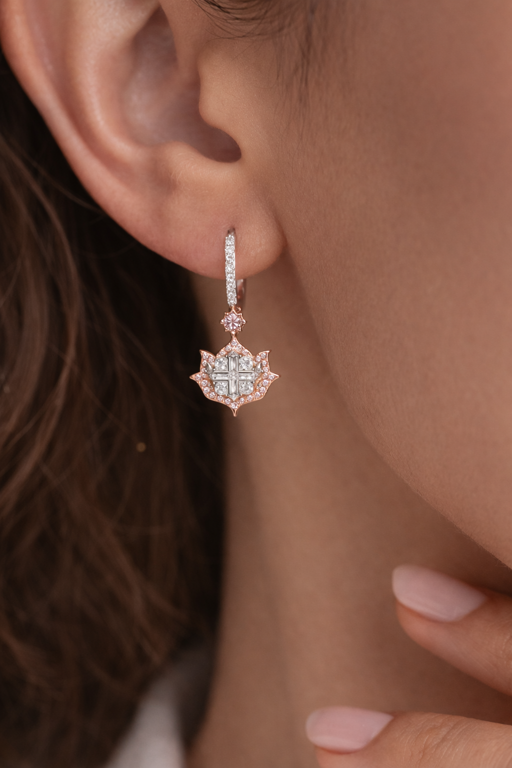 Close-up of a person wearing a rose gold earring with a diamond-like center.