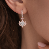 Close-up of a person wearing a rose gold earring with a diamond-like center.