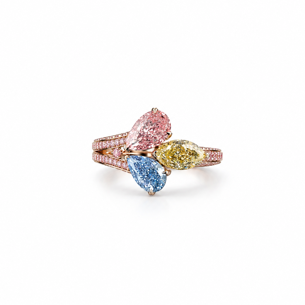 A three-stone diamond ring in rose gold, featuring a large pear-cut pink diamond, a marquise-cut blue diamond, and a round yellow diamond, with pavé-set diamonds along the rose gold band, shown on a plain white background.