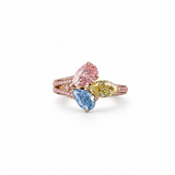 A three-stone diamond ring in rose gold, featuring a large pear-cut pink diamond, a marquise-cut blue diamond, and a round yellow diamond, with pavé-set diamonds along the rose gold band, shown on a plain white background.