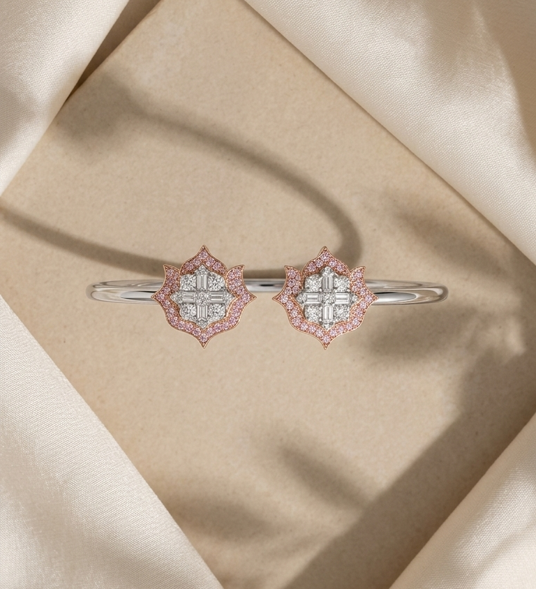 A pair of silver-toned bangle bracelets with diamond-like floral clusters accented by pink stones, displayed on a beige textured surface surrounded by draped cream satin fabric.