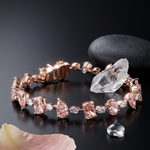 Rose gold bracelet with pink gemstones on a dark surface with a stone and flower petal.