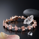 Rose gold bracelet with pink gemstones on a dark surface with a stone and flower petal.